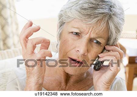 Stock Photo - Woman indoors using cellular phone frowning. Fotosearch