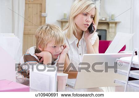 Woman using telephone in home office with laptop while young boy waits View Large Photo Image Stock Image - Woman using telephone in home office with laptop while young boy waits. Fotosearch