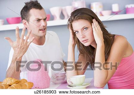 Stock Image - Young couple sitting at a table arguing. Fotosearch