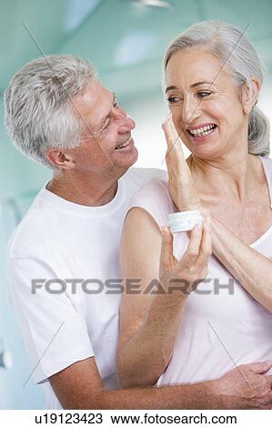 Stock Image - Couple embracing at a spa holding cream and smiling. Fotosearch