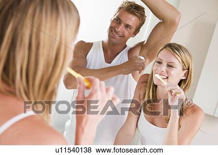Stock Photo - Couple in bathroom brushing teeth and applying deodorant. Fotosearch