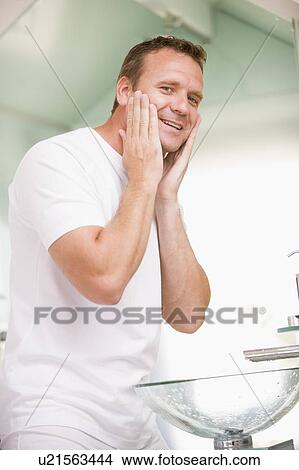 Picture - Man in bathroom applying aftershave and smiling. Fotosearch
