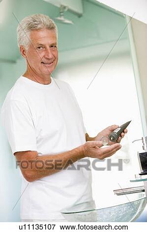 Stock Photo - Man in bathroom applying aftershave and smiling. Fotosearch