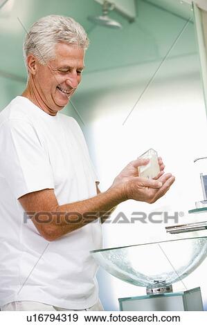 Stock Photo - Man in bathroom applying aftershave and smiling. Fotosearch
