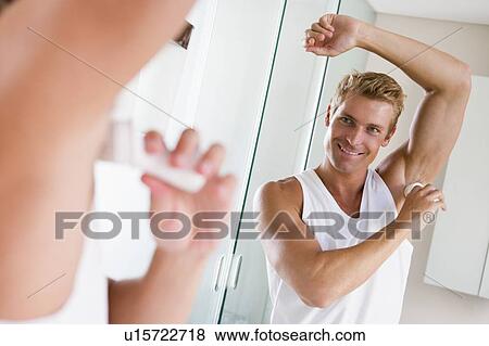 Stock Photo - Man in bathroom applying deodorant smiling. Fotosearch