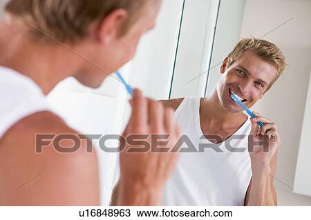 Stock Image - Man in bathroom brushing teeth and smiling. Fotosearch