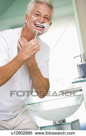 Stock Photography - Man in bathroom shaving and smiling. Fotosearch
