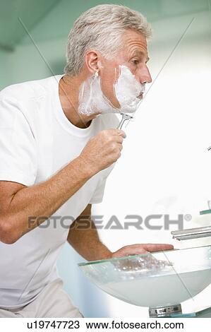 Stock Image - Man in bathroom shaving. Fotosearch