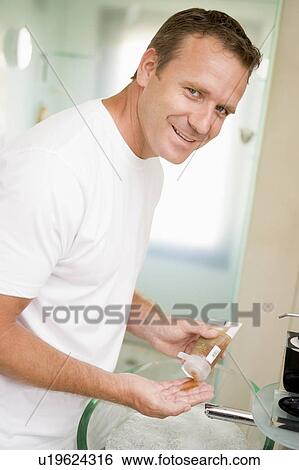 Stock Photograph - Man in bathroom with hair gel smiling. Fotosearch