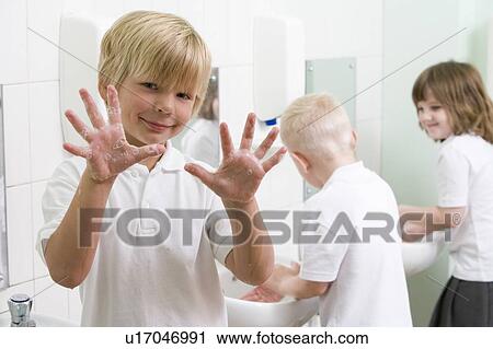 Stock Image - Students in bathroom at sinks washing hands with one holding up soapy hands (selective focus). Fotosearch