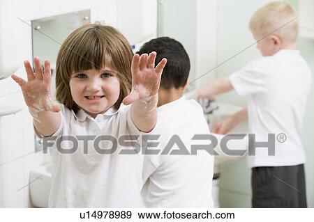 Stock Photo - Students in bathroom at sinks washing hands with one holding up soapy hands (selective focus). Fotosearch