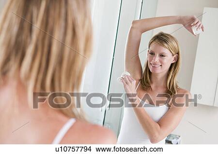 Picture - Woman in bathroom applying deodorant smiling. Fotosearch