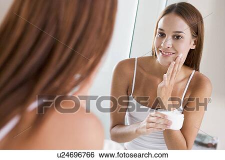 Stock Photograph - Woman in bathroom applying face cream smiling. Fotosearch