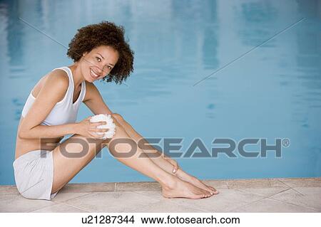 Woman sitting poolside using shower puff on leg smiling View Large Photo Image Picture - Woman sitting poolside using shower puff on leg smiling. Fotosearch