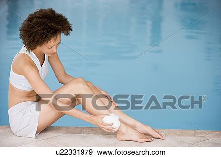Stock Photo - Woman sitting poolside using shower puff on leg. Fotosearch