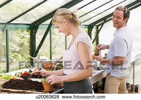 Stock Photo - Couple in greenhouse putting soil in pots smiling. Fotosearch