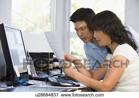 Stock Photo - Couple in home office with computer and paperwork pointing. Fotosearch