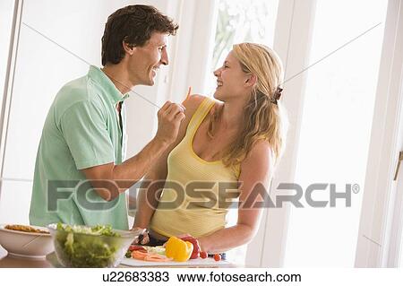 Stock Image - Couple in kitchen cutting up vegetables and smiling. Fotosearch