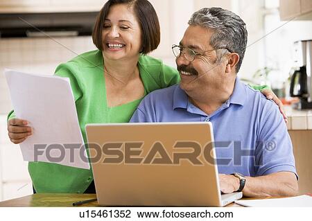 Couple in kitchen with laptop and paperwork smiling View Large Photo Image Stock Image - Couple in kitchen with laptop and paperwork smiling. Fotosearch