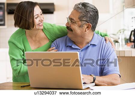 Couple in kitchen with laptop smiling View Large Photo Image Stock Photo - Couple in kitchen with laptop smiling. Fotosearch
