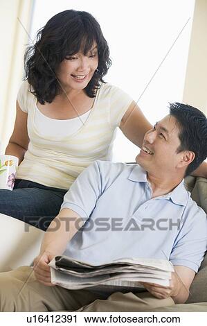 Stock Image - Couple relaxing with a newspaper and smiling. Fotosearch