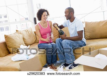 Couple relaxing with champagne by boxes in new home smiling View Large Photo Image Stock Image - Couple relaxing with champagne by boxes in new home smiling. Fotosearch
