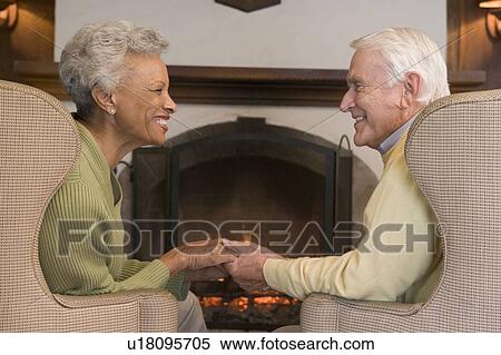 Couple sitting in living room by fireplace holding hands and smiling View Large Photo Image Stock Photography - Couple sitting in living room by fireplace holding hands and smiling. Fotosearch