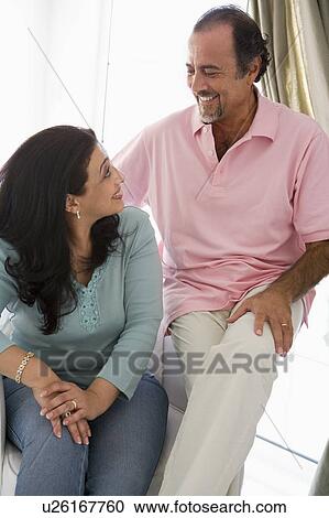 Stock Image - Couple sitting in living room smiling (high key). Fotosearch