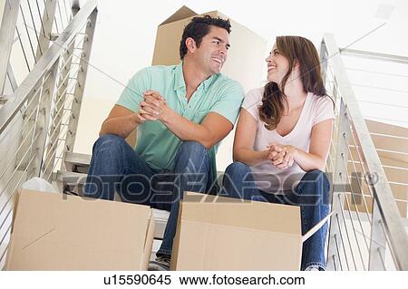 Stock Photography - Couple sitting on staircase with boxes in new home smiling. Fotosearch