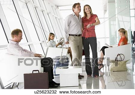 Stock Image - Couple waiting with other airline passengers in departure gate. Fotosearch