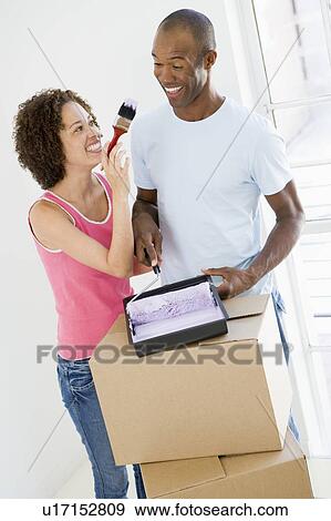 Couple with roller and paint in new home smiling View Large Photo Image Stock Photo - Couple with roller and paint in new home smiling. Fotosearch