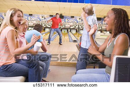 Stock Image - Family in bowling alley with two friends cheering and smiling. Fotosearch