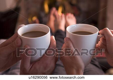 Stock Photograph - Feet warming at fireplace with hands holding coffee. Fotosearch