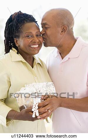 Husband and wife holding gift kissing and smiling View Large Photo Image Stock Image - Husband and wife holding gift kissing and smiling. Fotosearch