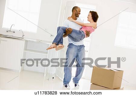Stock Photo - Husband holding wife in new home smiling. Fotosearch