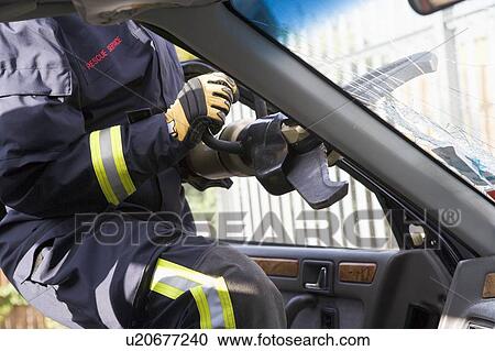 Stock Image - Firefighter cutting out a windshield after an accident. Fotosearch