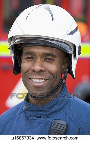 Picture - Fireman standing by fire engine wearing helmet. Fotosearch