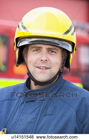 Stock Photo - Fireman standing by fire engine wearing helmet. Fotosearch