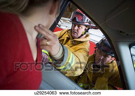 Stock Image - Fireman taking woman's pulse while another fireman watches (selective focus). Fotosearch