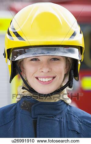 Stock Image - Firewoman standing by fire engine wearing helmet. Fotosearch