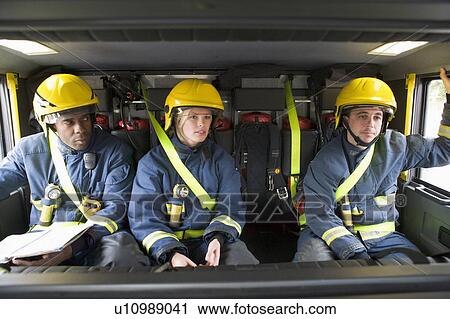 Three firefighters in fire engine wearing helmets with one reading View Large Photo Image Stock Image - Three firefighters in fire engine wearing helmets with one reading. Fotosearch