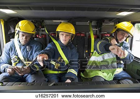 Stock Image - Three firefighters in fire engine wearing helmets with one pointing. Fotosearch