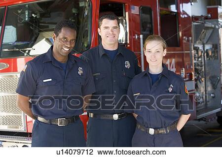 Stock Image - Three firefighters standing in front of fire engine. Fotosearch
