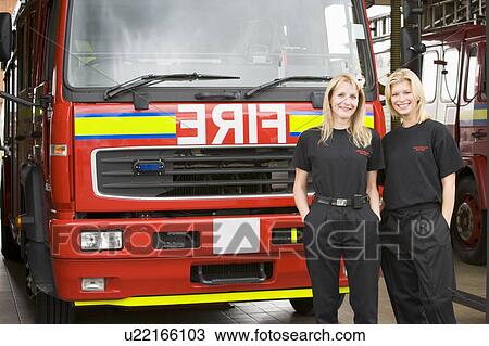 Stock Image - Two firefighters standing in front of fire engine. Fotosearch