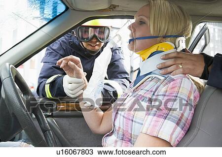 Stock Image - Two firemen helping a woman in neck brace breathe with oxygen mask. Fotosearch