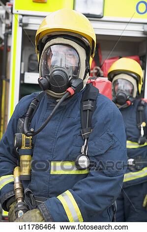Two firemen in masks standing near fire engine (depth of field) View Large Photo Image Picture - Two firemen in masks standing near fire engine (depth of field). Fotosearch