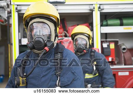 Stock Image - Two firemen in masks standing near fire engine (depth of field). Fotosearch