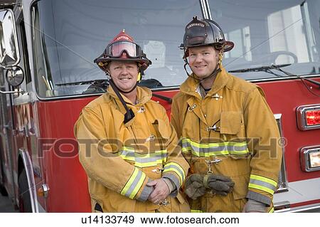 Stock Photo - Two firemen standing in front of fire engine. Fotosearch