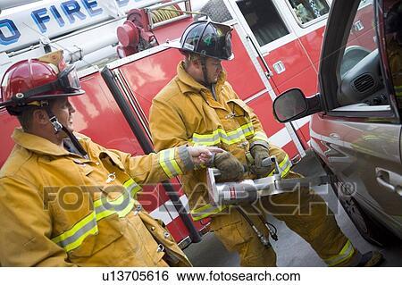 Stock Photograph - Two firemen using the jaws of life on a car door. Fotosearch