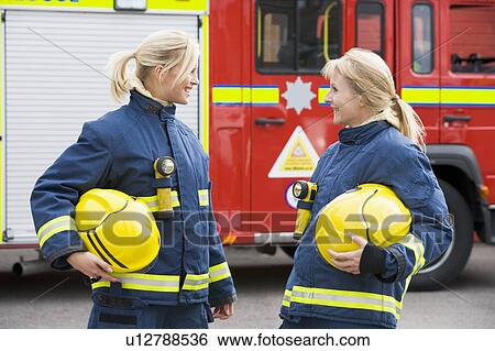 Two firewomen standing by fire engine talking View Large Photo Image Stock Photograph - Two firewomen standing by fire engine talking. Fotosearch